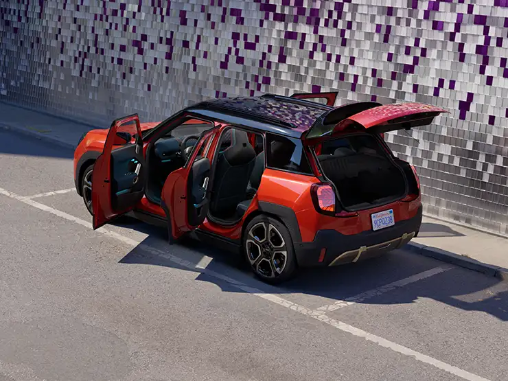 MINI Aceman in Sunset Orange Metallic parked with all doors and tailgate open beside a tiled wall.