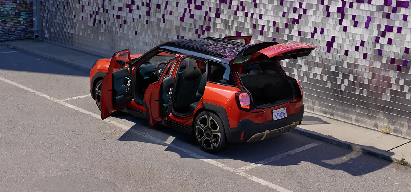 MINI Aceman in Sunset Orange Metallic parked with all doors and tailgate open beside a tiled wall.