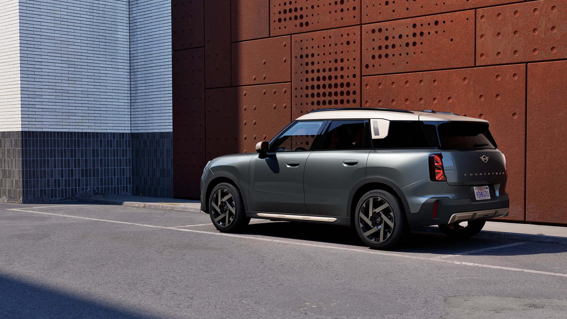 Vue arrière trois quarts d’un MINI Countryman stationné à côté d’un mur perforé de couleur rouille.